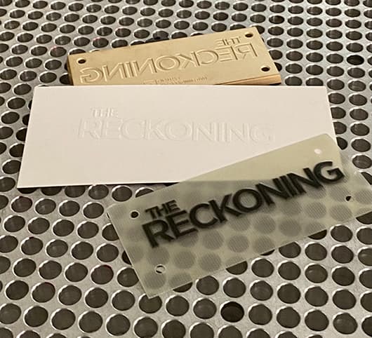 A clear polymer plate, an embossed white proof, and a brass die laid out together on a steel bench