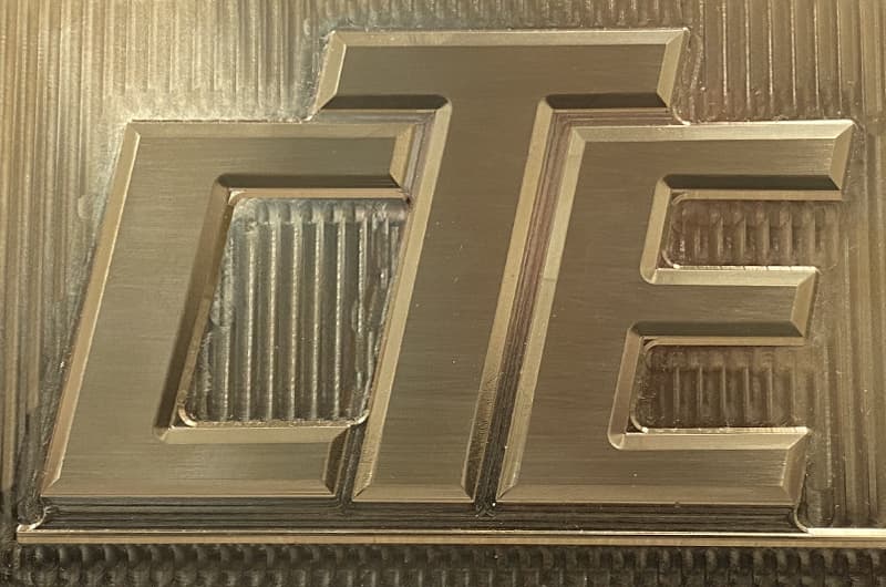 Machined brass emboss die with a raised letterform and textured field