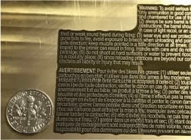 Brass foil stamping die carrying dense warning-label text, a coin beside it for scale